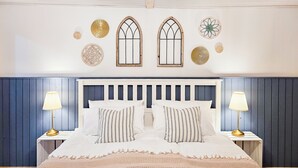 Een slaapkamer met een wit bed, twee nachtkastjes, een houten hoofdbord en decoratieve wandkunst.