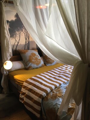 Una cama con cubrecama a rayas, dosel y almohadas con estampado de hojas de palmera.