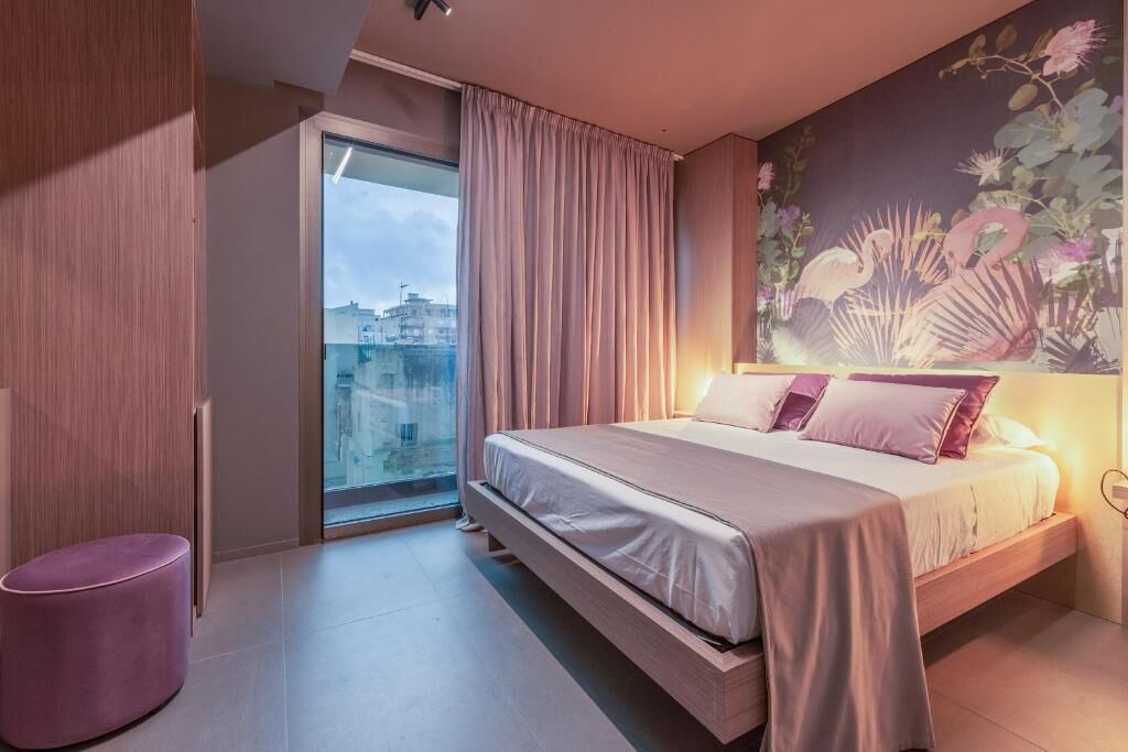 A modern bedroom with a large bed, a sliding glass door to a balcony, and a floral mural on the wall.