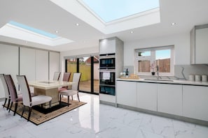 A modern kitchen with a skylight, a dining area with a glass table, and a view of the outside. - Stunning 5 Bedroom, 3 Bathroom Home in Windsor (Windsor)
