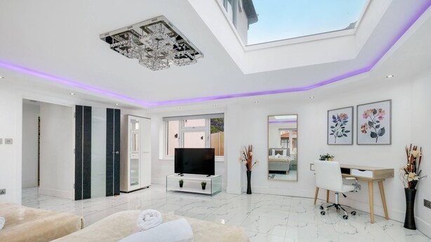 A modern spa room with a skylight, a TV, massage tables, and a desk with a chair.