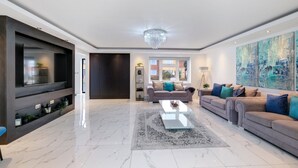 A modern living room with a large flat-screen TV, a sofa set, a coffee table, and a chandelier.