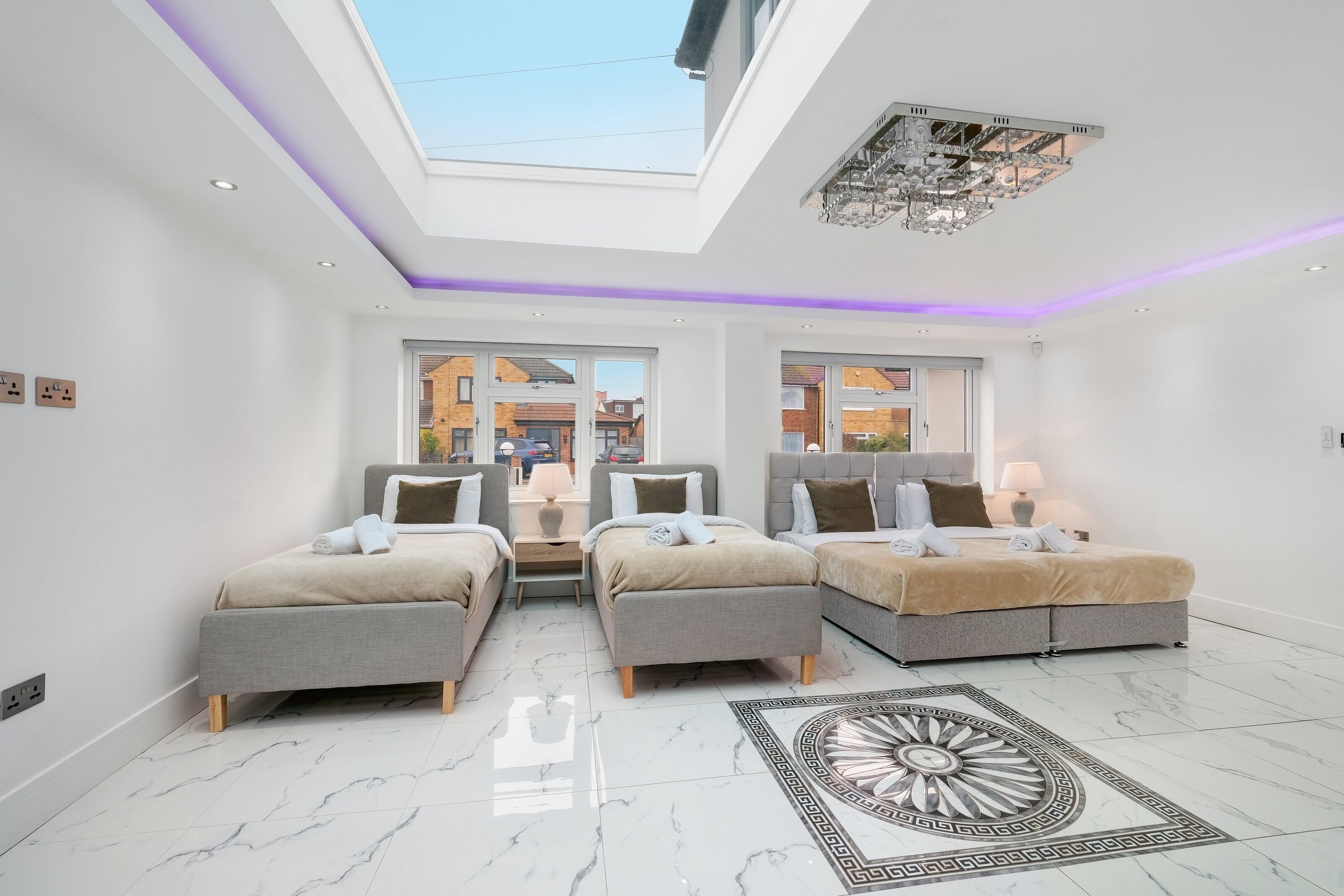 A modern bedroom with two beds, a skylight, and a chandelier.