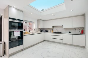 A modern kitchen with a skylight, white cabinets, a black oven, and a marble floor. - Stunning 5 Bedroom, 3 Bathroom Home in Windsor (Windsor)