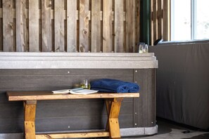 Un banc de fusta amb un llibre i un got d'aigua davant d'una banyera d'hidromassatge.