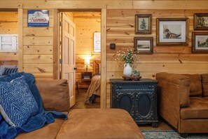 Interior acollidor d'una cabana de fusta amb un sofà de cuir marró, una manta blava i un ràdio antic sobre una taula auxiliar de fusta.