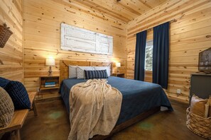 Habitació de cabana de fusta amb un llit, taules de nit, una làmpada i vista a l'exterior.
