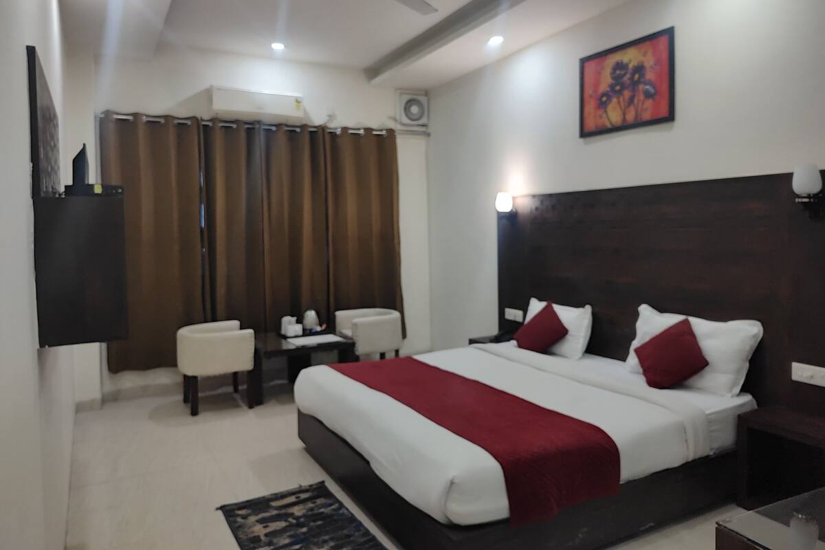A hotel room with a large bed, a desk, a chair, a TV, and a ceiling fan.