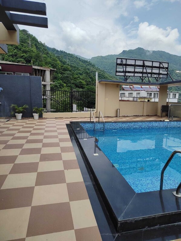 Ein Schwimmbecken mit Schachbrettmuster, umgeben von einem Zaun und Topfpflanzen.