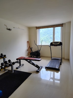 A gym with a treadmill, elliptical, bench press, and dumbbells. - Foxoso Heights Tapovan (Rishikesh)
