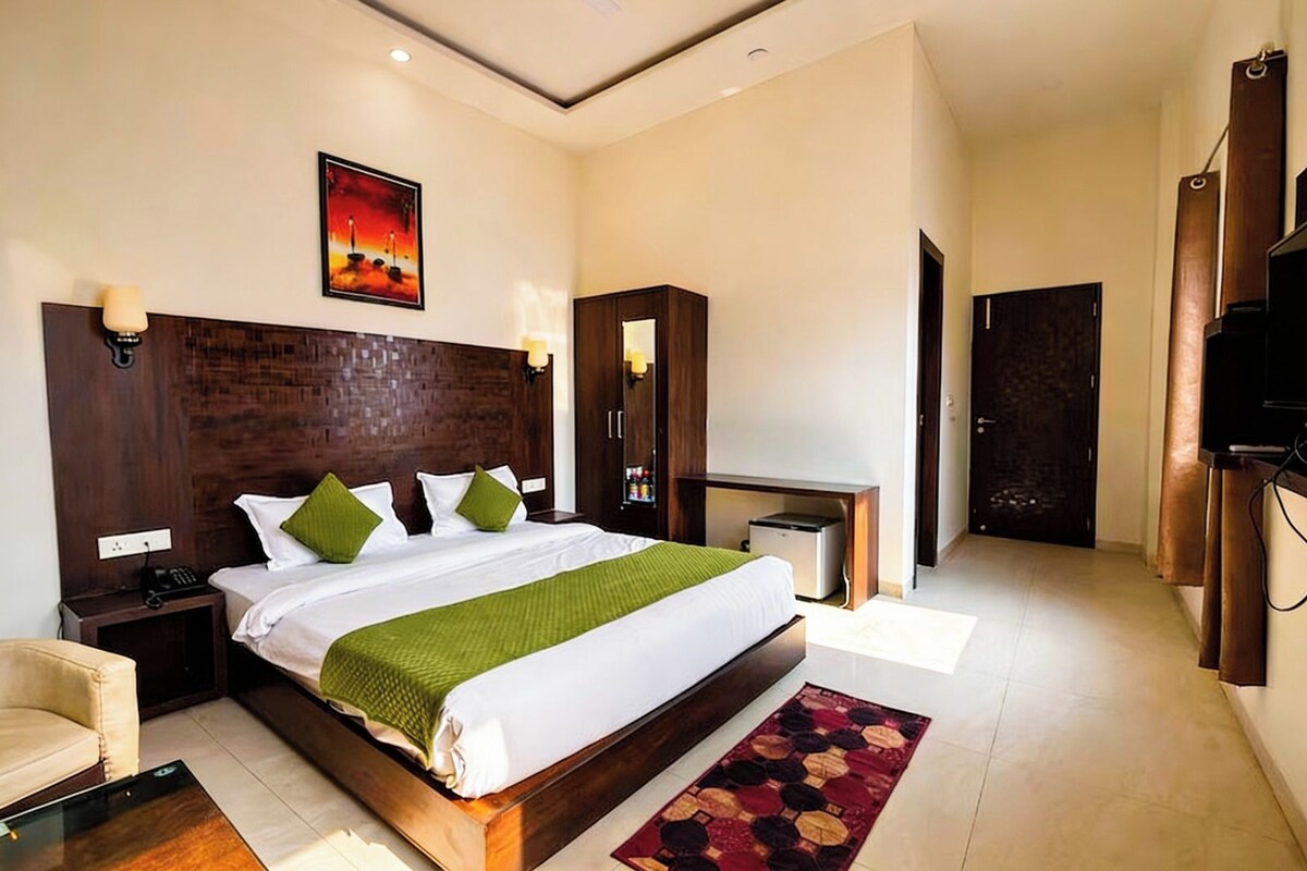 A modern hotel room with a large bed, bedside tables, a desk, a TV, and a door.