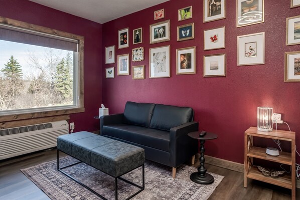 A room with a dark sofa, a small table, a bench, and a wall adorned with framed pictures. - Girls’ Getaway | Free Parking | Simple Comfort (Prescott)
