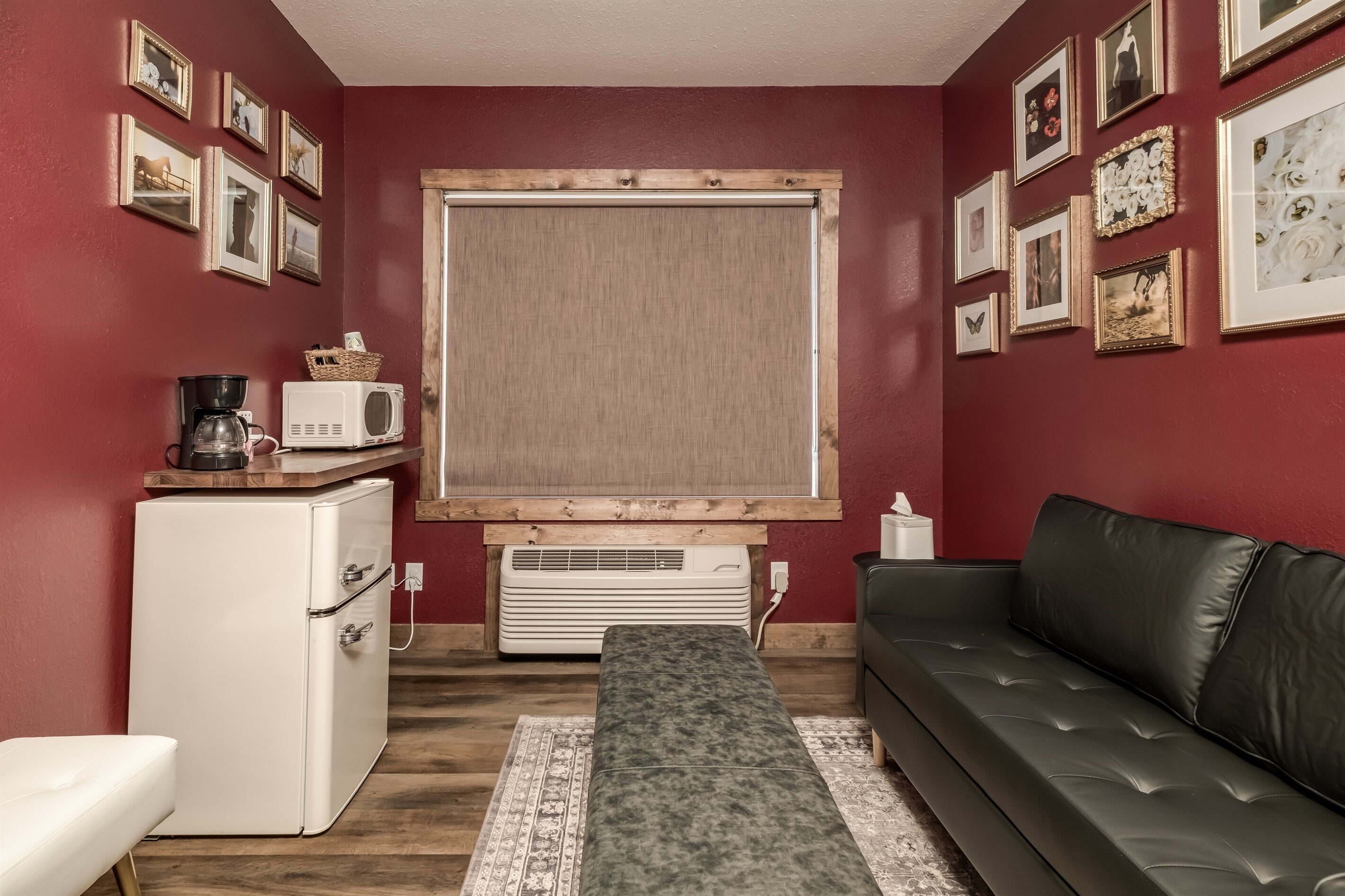 Un espacio habitable compacto con kitchenette, un sofá, un banco y un ventanal grande con persianas.