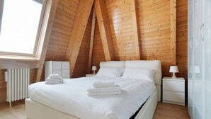 Ein Schlafzimmer mit schrägem Dach, einem Bett mit weißen Leinen, zwei Nachttischen mit Lampen und einem Heizkörper.