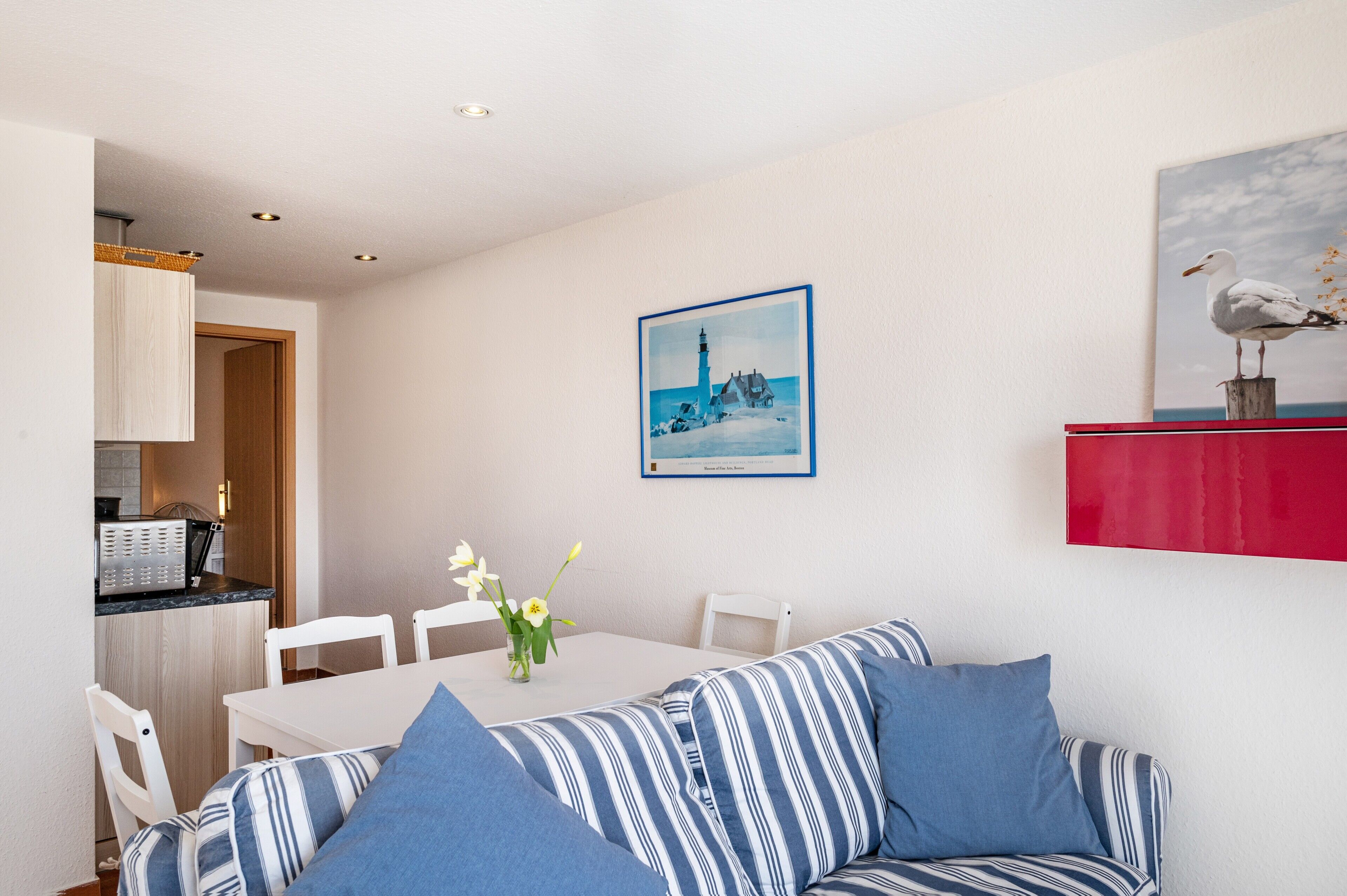 Una habitación con un sofá a rayas, una mesa de comedor con sillas, una zona de cocina y un cuadro en la pared.