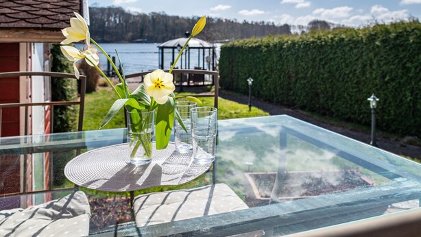 Une table avec un plateau en verre, un vase rempli de fleurs et quatre verres.