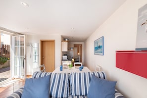 Ein modernes Wohnzimmer mit einer Couch, einem Esstisch mit Stühlen, einer Küchenzeile und einem roten Schrank.