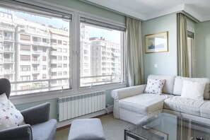 A living room with a white sofa, a glass coffee table, and a view of a cityscape through large windows. - Koxka - Basque Stay (San Sebastián)
