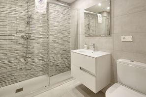 A modern bathroom with a glass shower enclosure, a white sink, and a toilet. - Koxka - Basque Stay (San Sebastián)