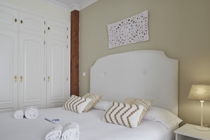 A hotel room with a large bed, white curtains, a wooden column, a decorative wall piece, and a bedside table with a lamp. - Bengoetxea - Basque Stay (San Sebastián)