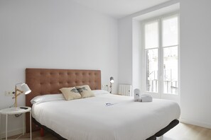 A bedroom with a large bed, white walls, a window, and a bedside table with a lamp. - Etxaide - Basque Stay (San Sebastián)