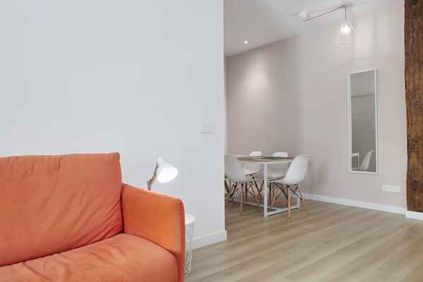 Un moderno salón con un sofá, una zona de comedor con mesa y sillas, y un espejo grande en la pared.