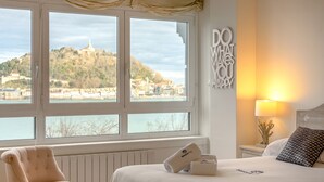 A bedroom with a large window, a bed with white bedding, a chair, and a wall with a motivational quote. - Maskortxo - Basque Stay (San Sebastián)