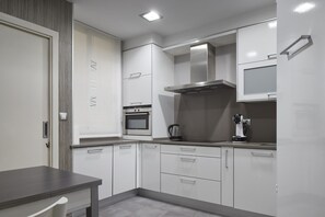 A modern kitchen with white cabinetry, a built-in oven, and a stainless steel range hood. - Ordulari - Basque Stay (San Sebastián)