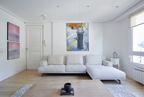 A modern bedroom with a white sofa, a painting of a fire hydrant, and a view of the city through the window. - Arraun - Basque Stay (San Sebastián)