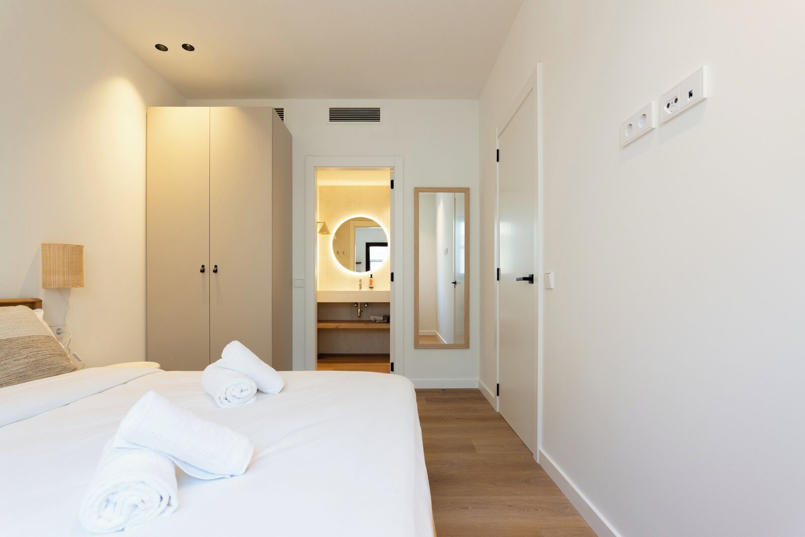 A hotel room with a bed, a wardrobe, a bathroom with a mirror, and a light fixture.