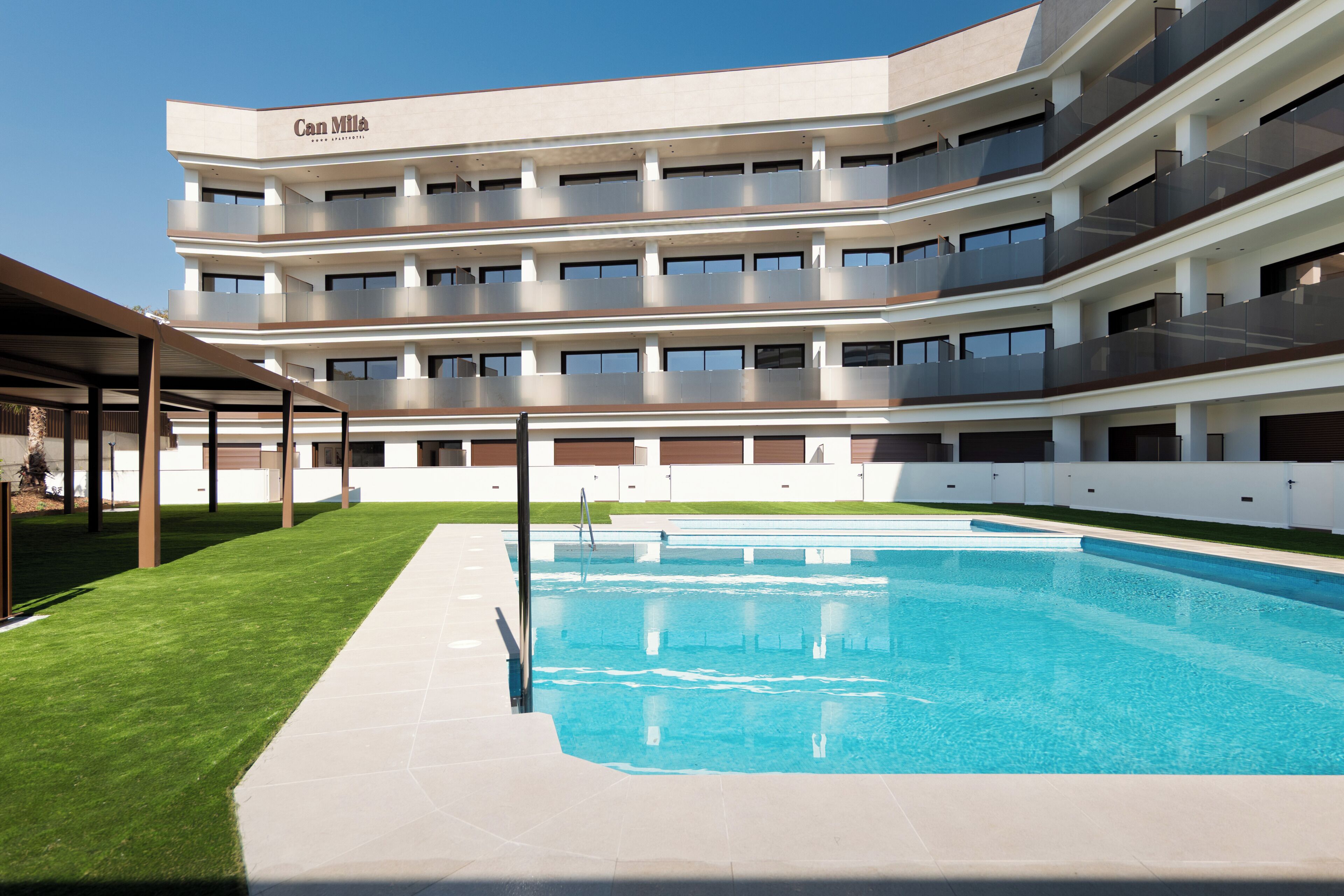 A multi-story hotel with a swimming pool, outdoor seating area, and a well-maintained lawn.