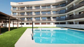 A multi-story hotel with a swimming pool, outdoor seating area, and a well-maintained lawn.