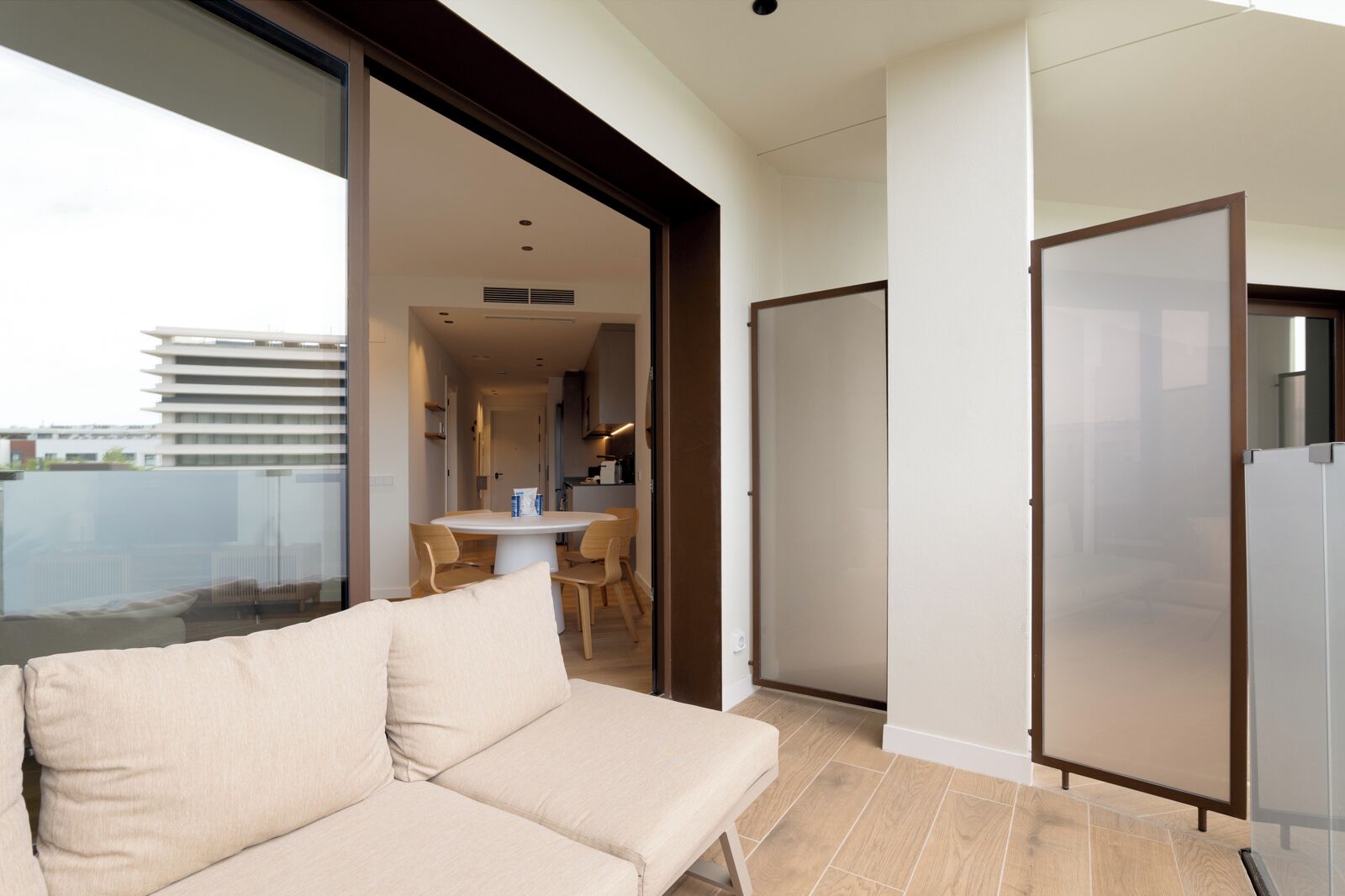 A modern living room with a sofa, a dining table with chairs, and a kitchen area visible through an open door.