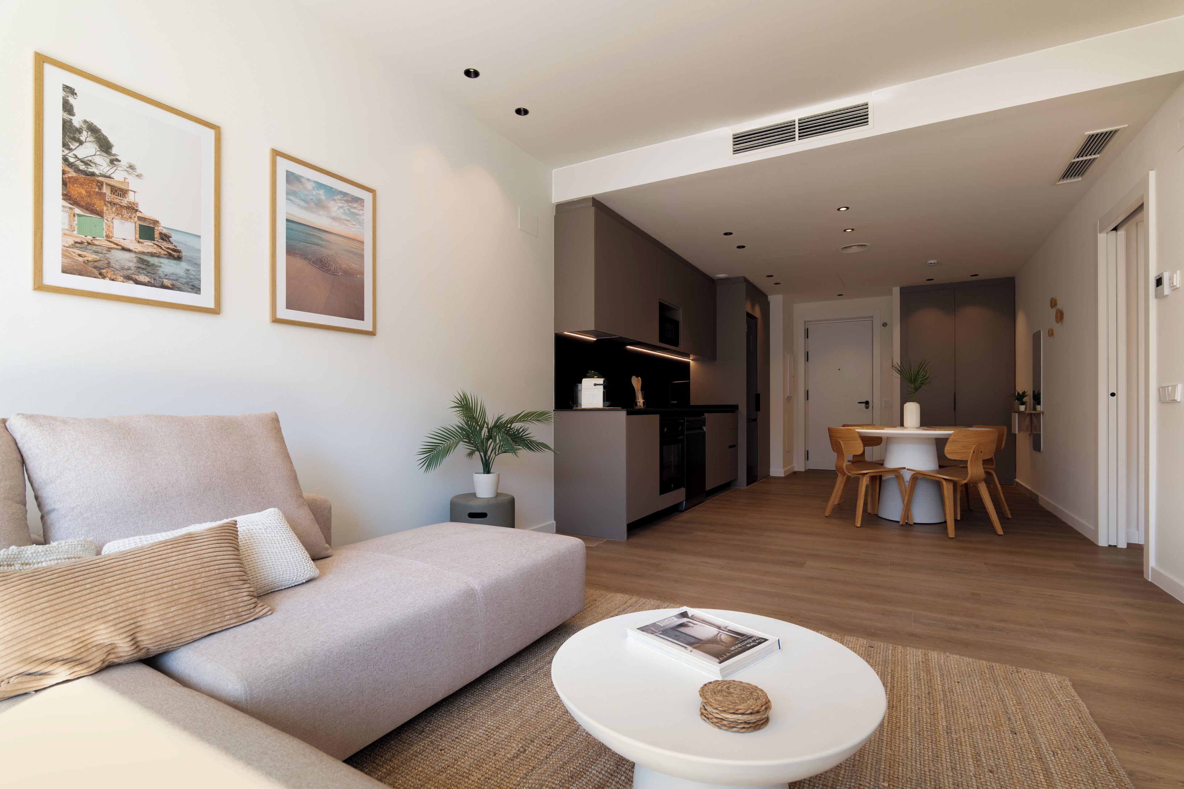 Ein modernes Wohnzimmer mit einer Couch, einem Esstisch mit Stühlen, einer Küchenzeile und gerahmten Bildern an der Wand.