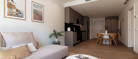 Ein modernes Wohnzimmer mit einer Couch, einem Esstisch mit Stühlen, einer Küchenzeile und gerahmten Bildern an der Wand.