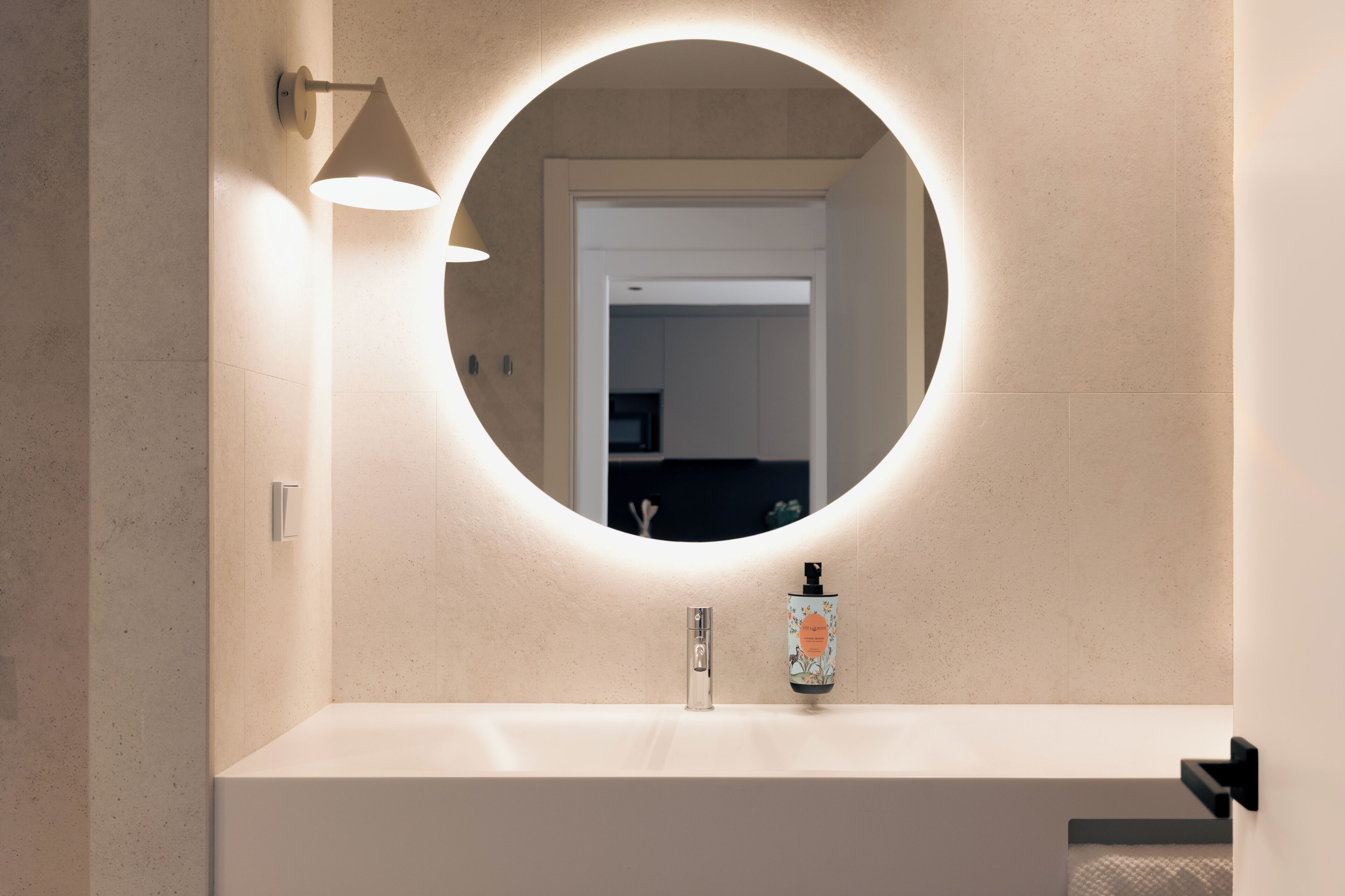 A bathroom with a round mirror, a modern faucet, and a bottle of shampoo.