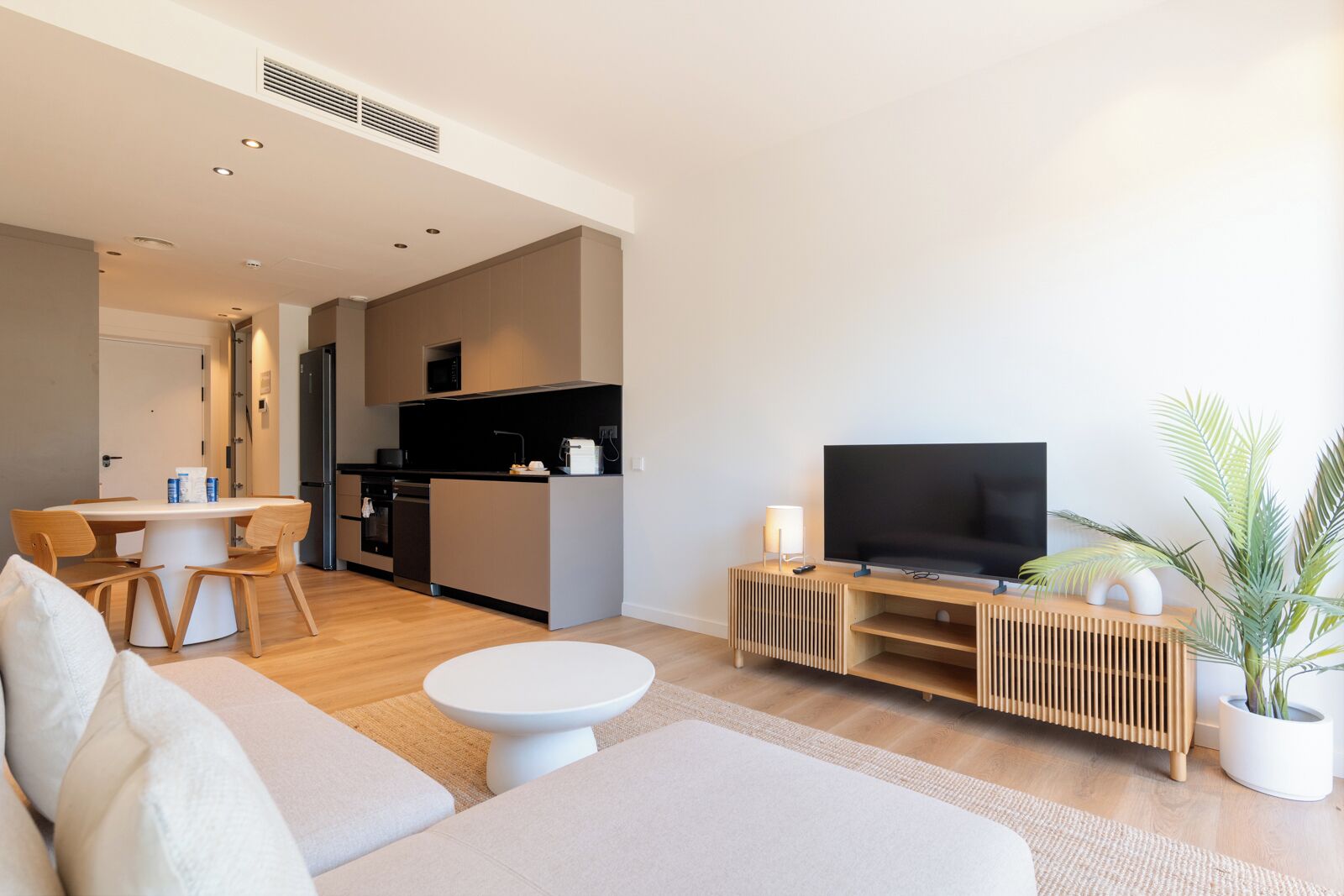 Un salon moderne comprenant un canapé, une table à manger, un coin cuisine et un téléviseur posé sur un meuble en bois.