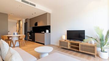 Una sala de estar moderna con un sofá, una mesa de comedor, una zona de cocina y un televisor sobre un mueble de madera.