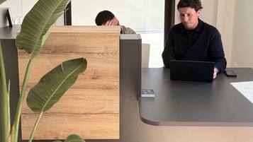 A reception desk with a laptop, a smartphone, and a wooden panel.