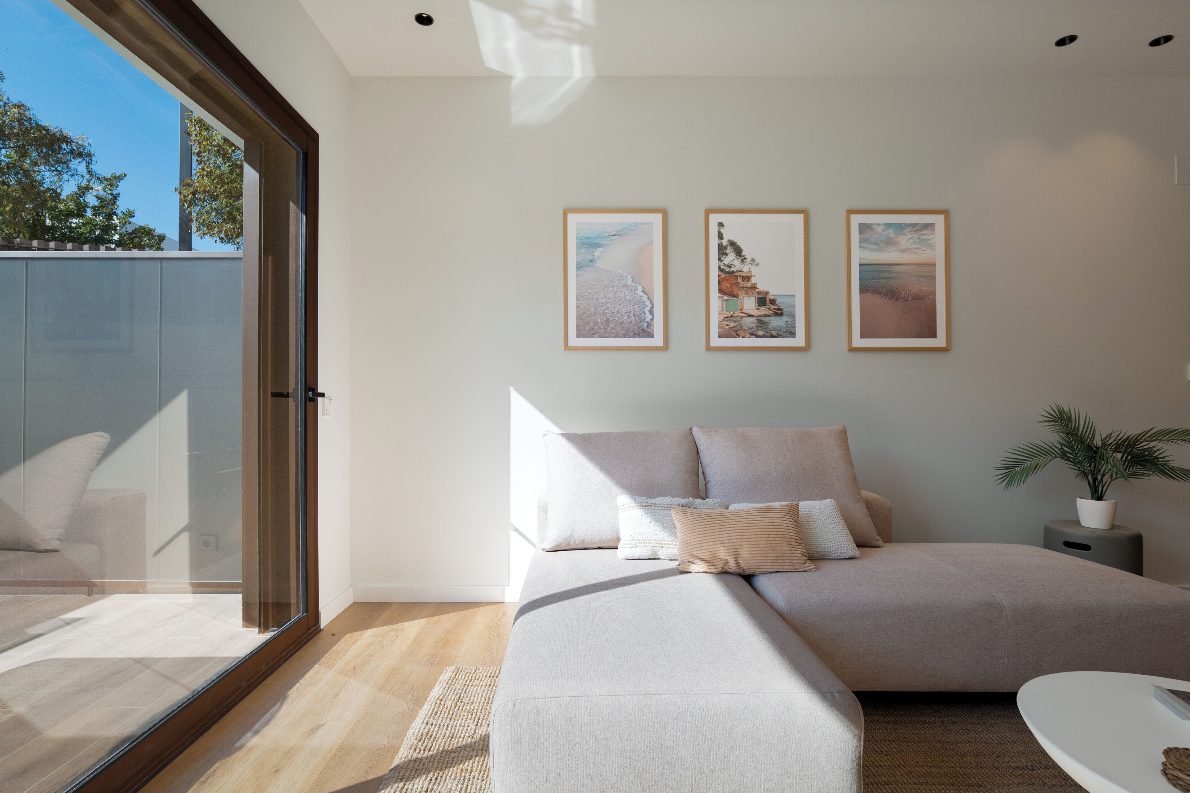 Un salon moderne avec un grand canapé, une table basse et une plante en pot. Trois tableaux encadrés ornent le mur.