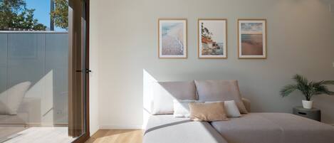 A modern living room with a large sofa, a coffee table, and a potted plant. There are three framed pictures on the wall.