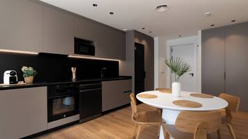 Una cocina moderna con electrodomésticos integrados, un comedor con mesa y sillas redondas, y una puerta que da a otra habitación.