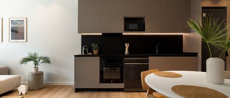 A modern kitchen with built-in appliances, a dining area with a white table and placemats, and a potted plant.