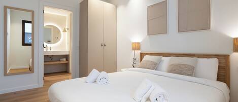 Una habitación de hotel moderna con una cama grande, un baño con espejo y lavamanos, y un armario.
