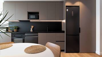 A modern kitchen with a built-in microwave, a stainless steel refrigerator, and a dining area with a white table and woven placemats.