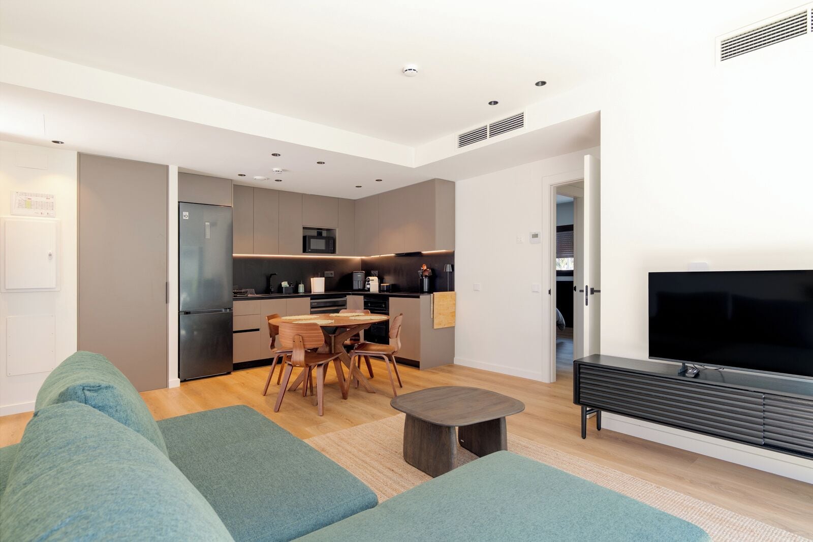 A modern living room with a sofa, a TV, and a dining area with a table and chairs.