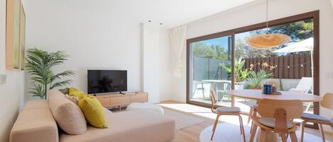 A living room with a sofa, TV, dining table, chairs, and a large sliding glass door to an outdoor area.