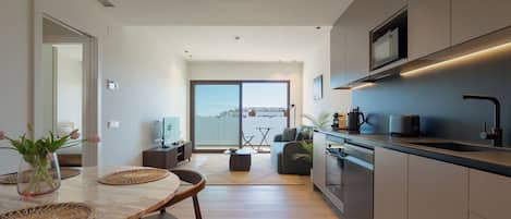 A modern kitchen with a dining area, a sofa, and a view through a sliding door.