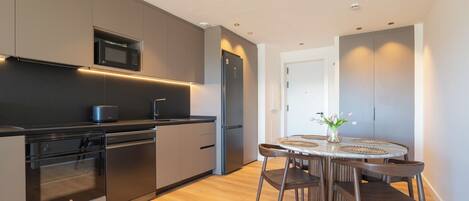 Una cocina moderna con electrodomésticos integrados, un comedor con mesa redonda y sillas, y piso de madera.
