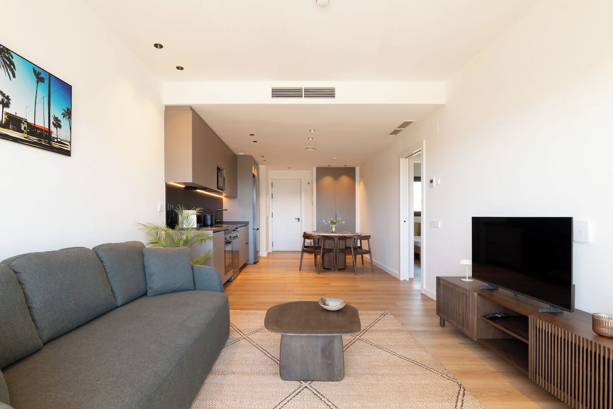 Una sala de estar moderna con un sofá, una mesa de centro, un televisor y un comedor con una mesa y sillas.